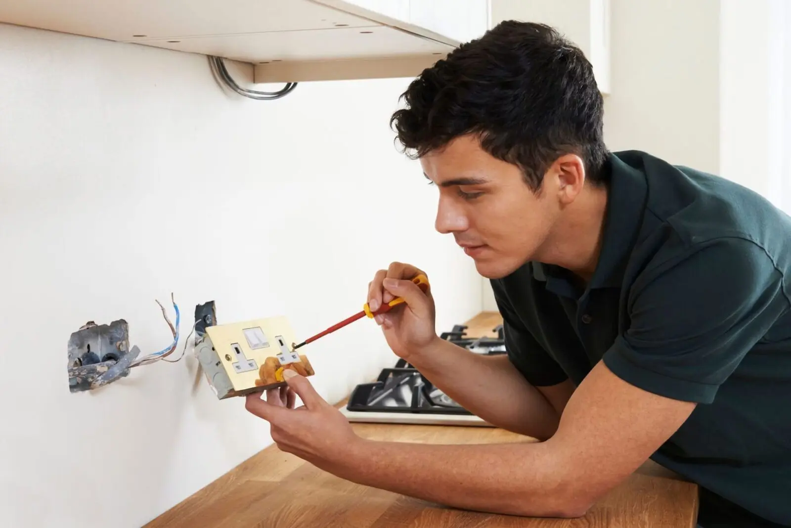 A man performing a do-it-yourself project in a kitchen by working on a light switch.