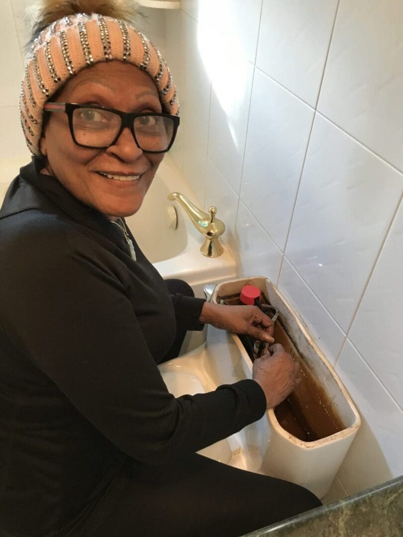 A person looking at the camera and repairing a toilet bowl