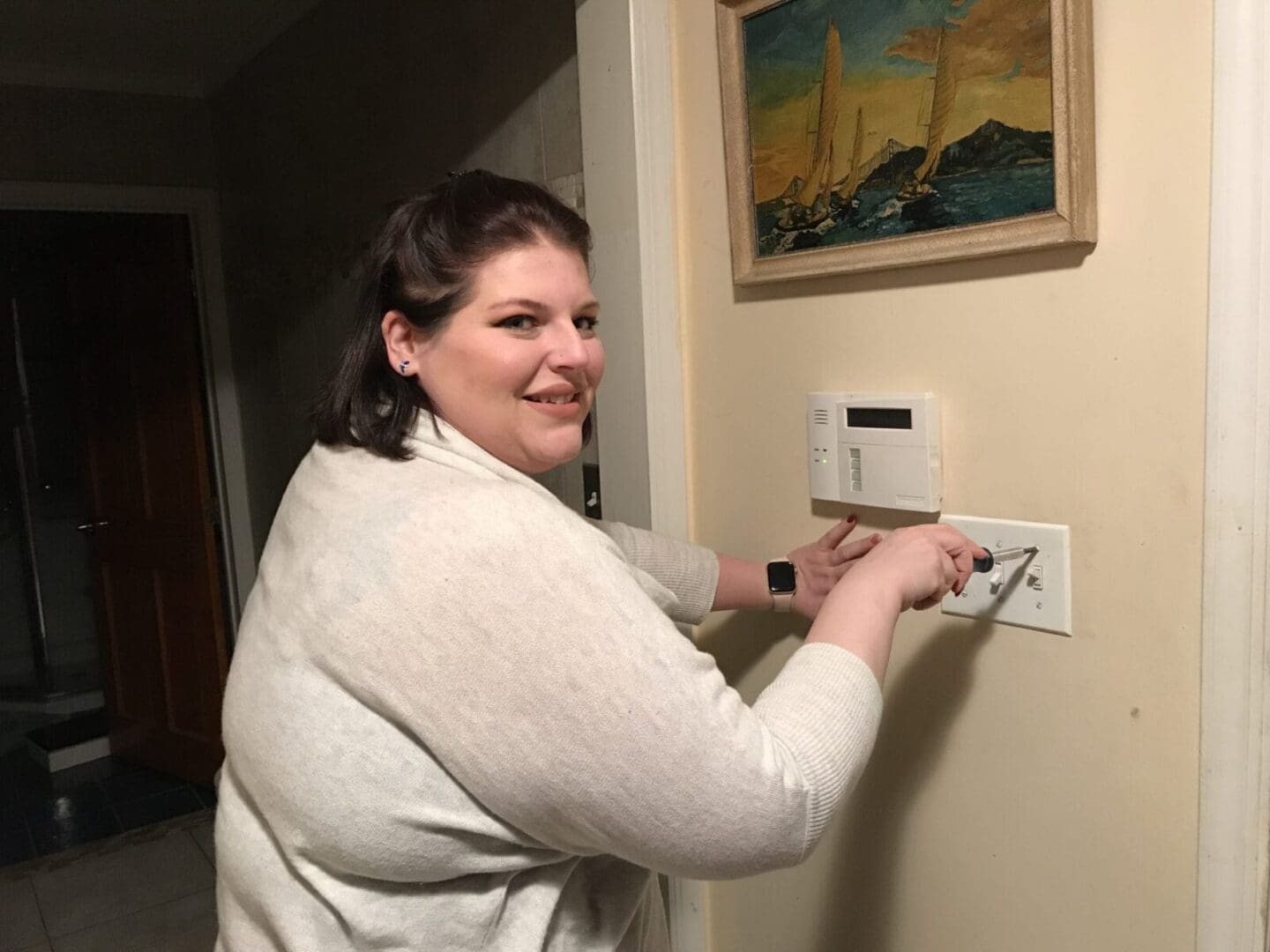 A person looking at the camera while holding a screwdriver and repairing a wall socket