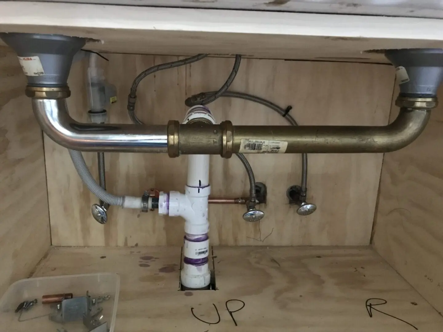 A sink under a wooden cabinet with pipes and pipes.