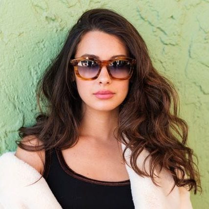 A woman wearing sunglasses leaning against a wall.