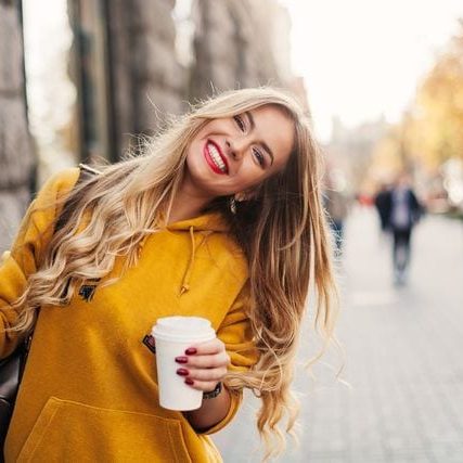 A young woman holding a cup of coffee while walking down the street.